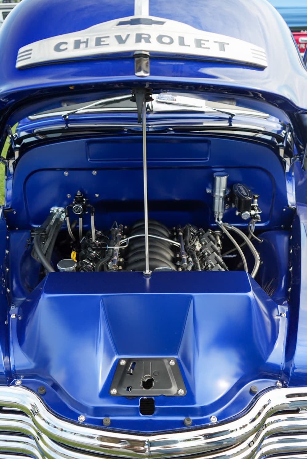 Conrad Captures photograph: engine bay of a royal-blue classic Chevrolet truck with the hood open and Chevrolet bowtie emblem.