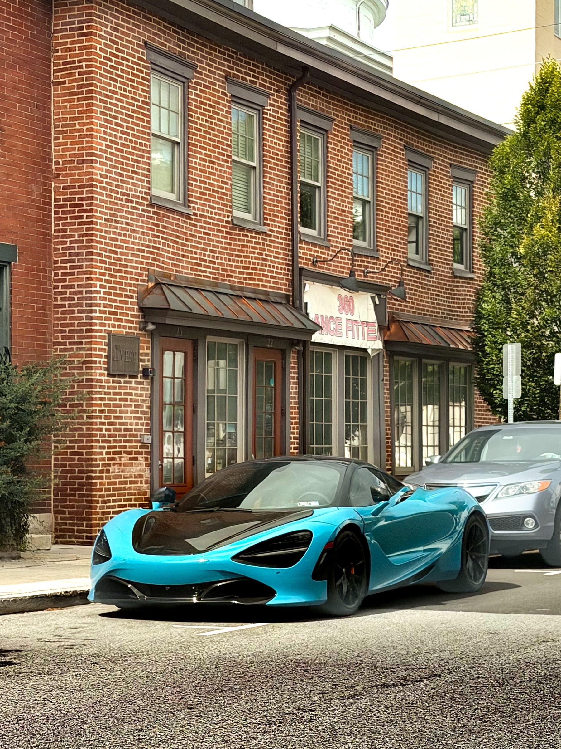 Conrad Captures photograph: cyan and black McLaren 720S parked on a brick street in front of a red brick building.